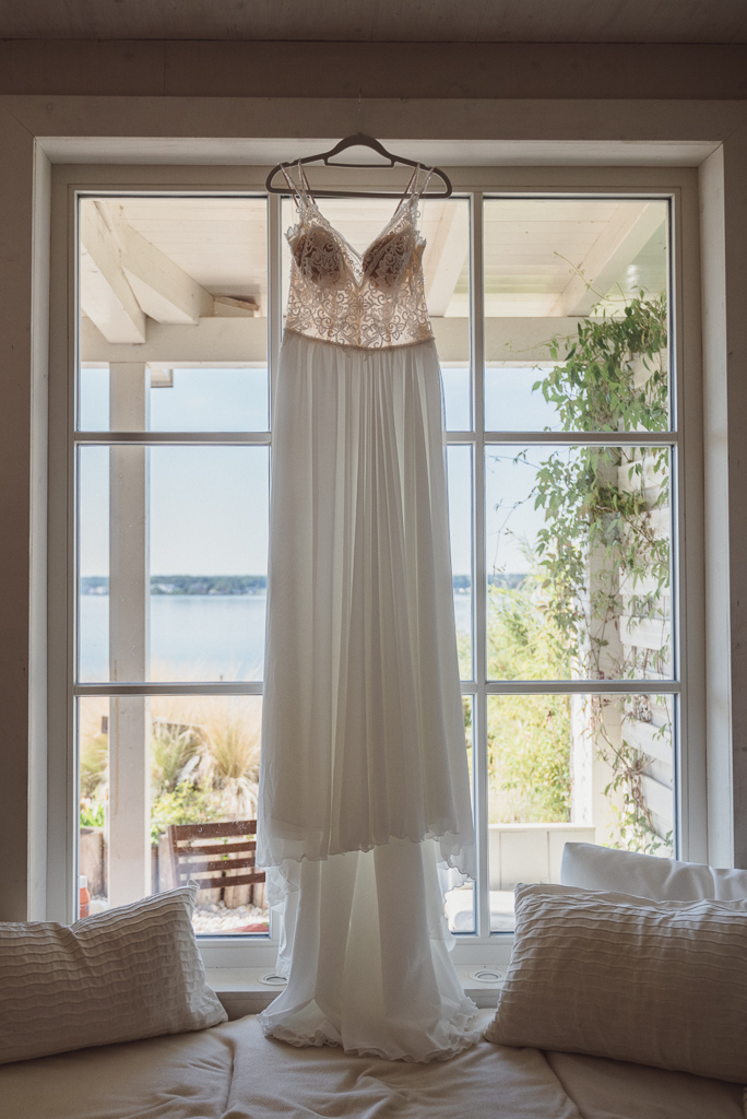 Das Brautkleid hängt vor einem großen Fenster mit Blick auf den Hainer See.