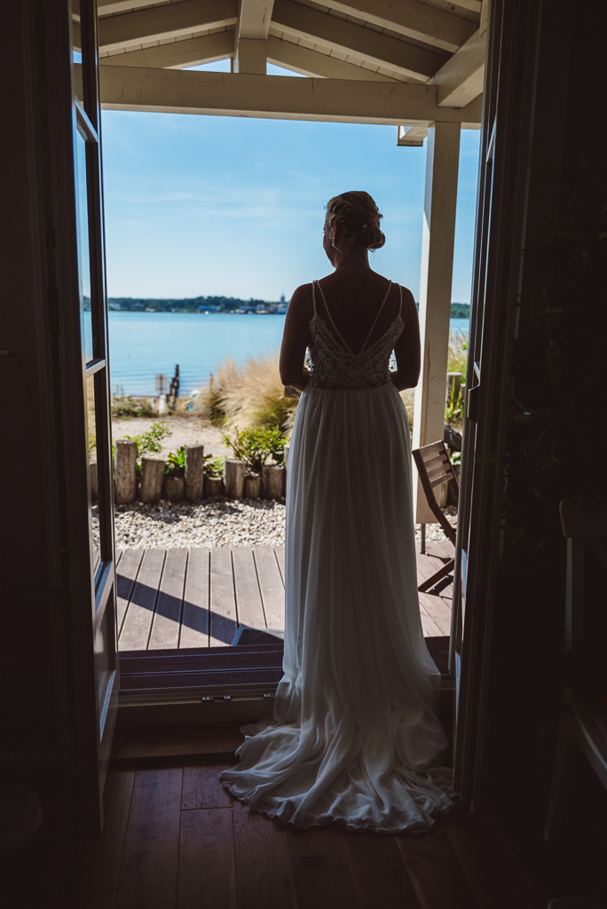 Braut steht in der Terrassentür und schaut Richtung Hainer See. Foto von hinten.