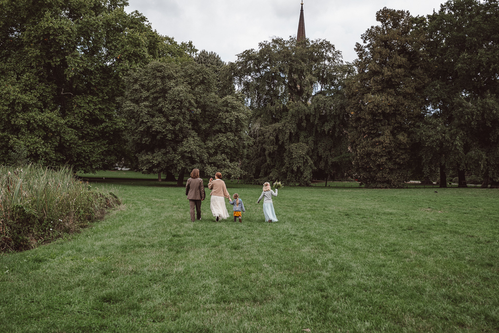 Brautpaar und die beiden Kinder laufen über eine große Wiese. Man sieht sie von hinten.