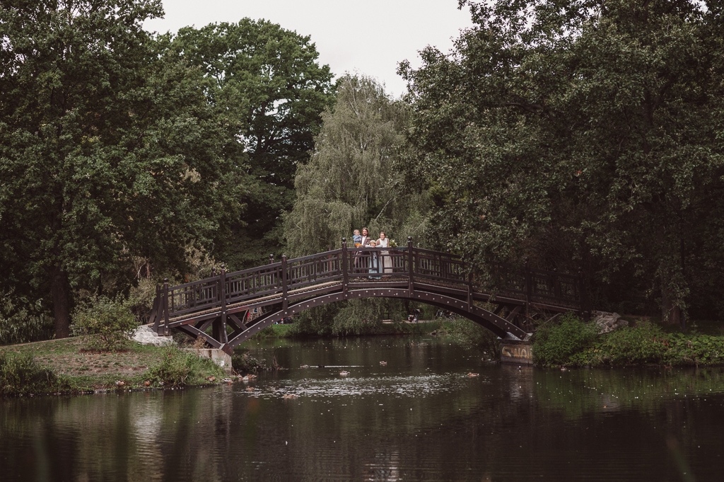 Brautpaar und Kinder stehen auf einer Holzbrücke im Johannapark Leipzig. man sieht sie nur ganz klein.