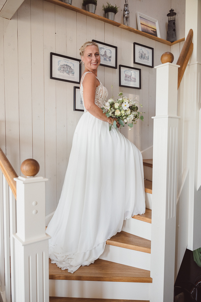 Portraitfoto der Braut auf der Treppe der weißgehaltenen Ferienwohnung.