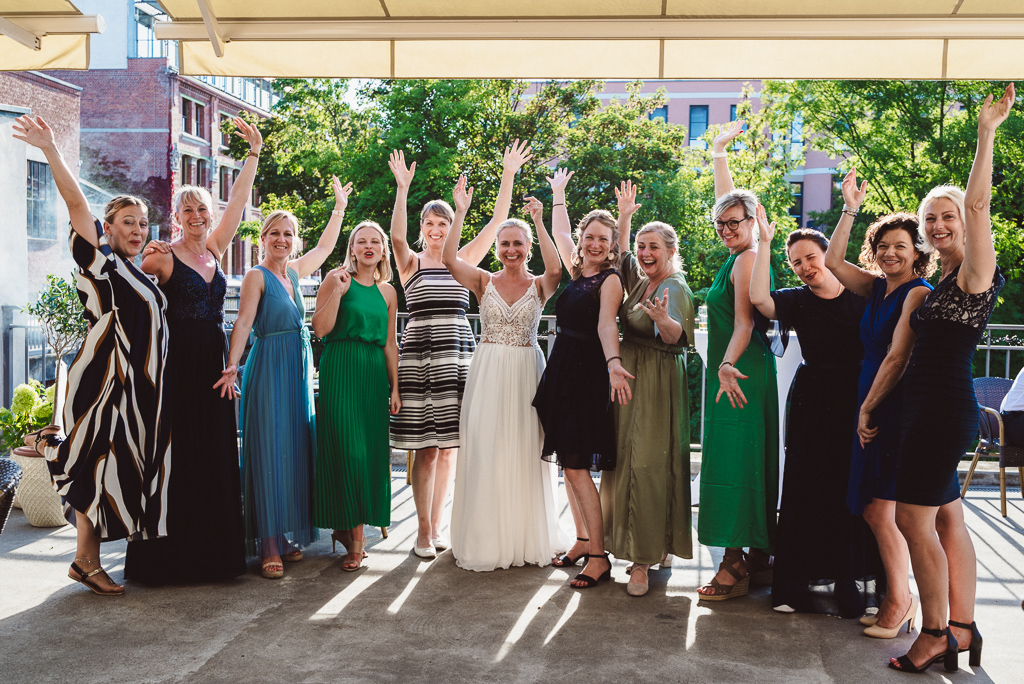 Gruppenfoto der Frauen. Neun Frauen lachen in die Kamera, Arme in der Luft, die Braut steht in der Mitte.