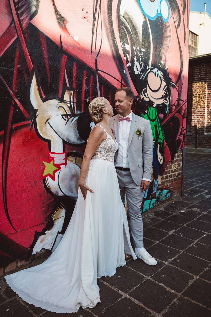 Portraitfoto des Brautpaares vor einer Graffitiwand