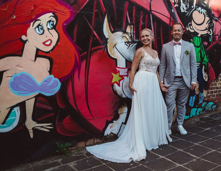 Portraitfoto des Brautpaares vor einer Graffitiwand