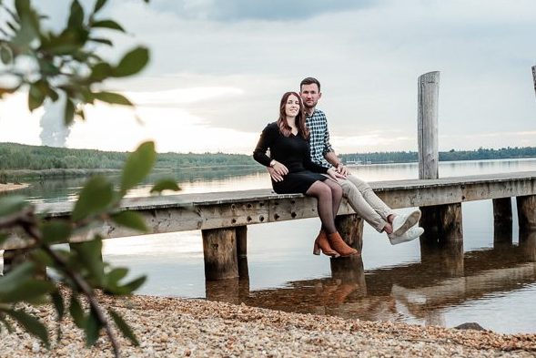 Foto vom Fotoshooting eines Paares auf einem Steg sitzend, um Fotos ihrer Lovestory festzuhalten