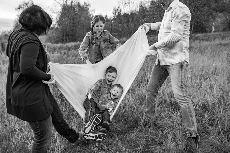 Schwarzweißbild von einem Familienfotoshooting, bei dem die Kinder mit einer Decke geschaukelt werden.