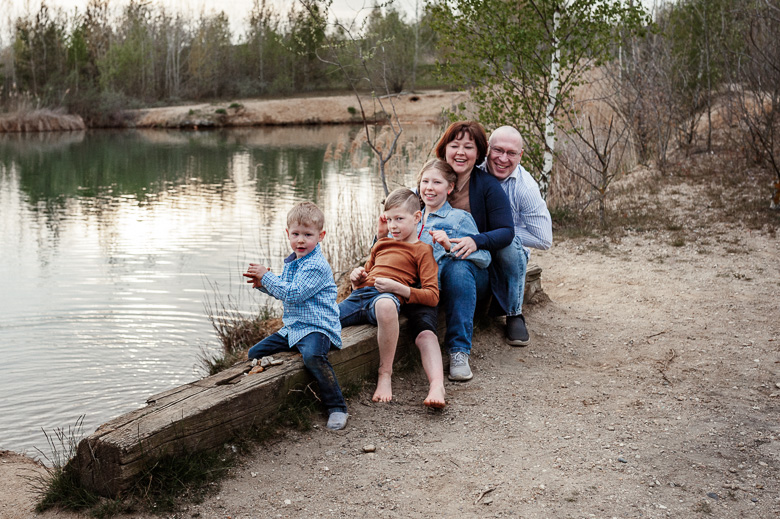 Fröhliche fünfköpfige Familie sitzt am See hintereinander beim Fotoshooting in Störmthal