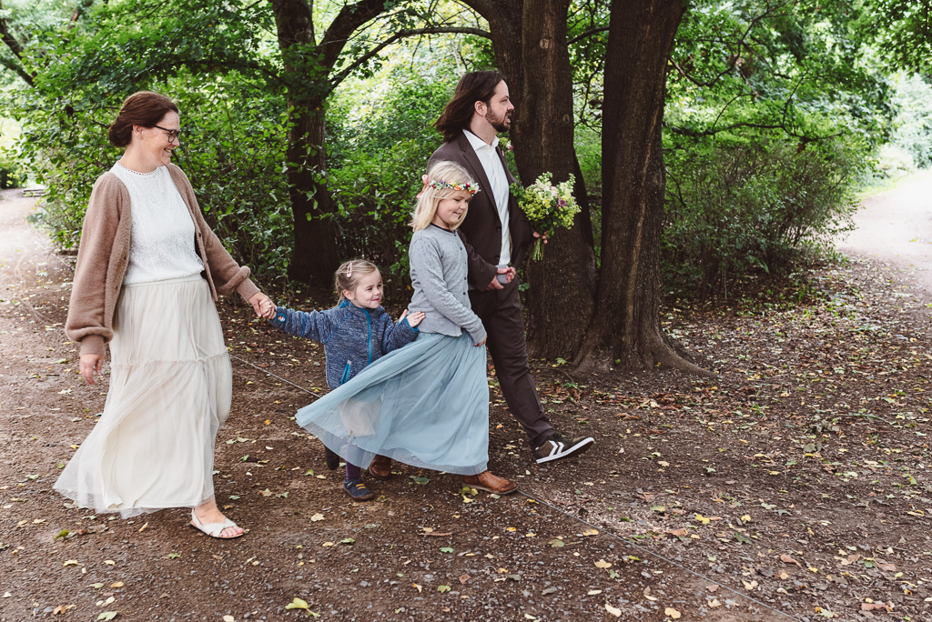 Brautpaar und ihre Kinder laufen gemeinsam Hand in Hand durch den Johannapark