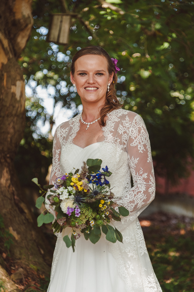 Portraitfotos einer Braut mit Brautstrauß in der Natur vor eienm großen alten Baum. Frontales Profilfoto