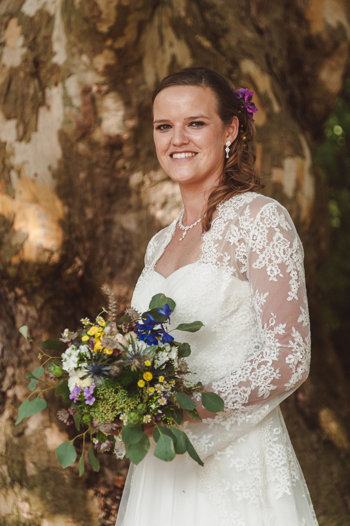 Portraitfotos einer Braut mit Brautstrauß in der Natur vor eienm großen alten Baum. Seitliches Profilfoto