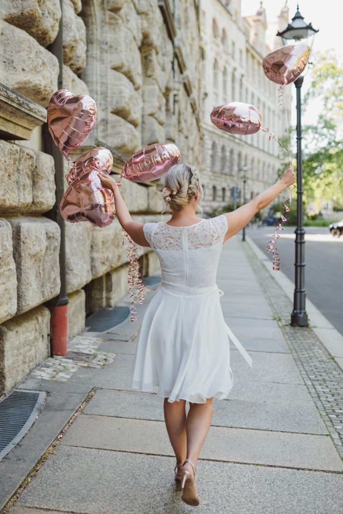 Braut in Rückenansicht vor dem Standesamt Leipzig mit Herz Luftballons in der Hand